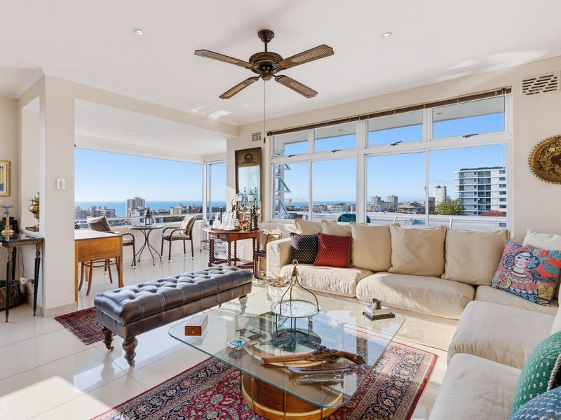 Spacious living room featuring large windows with expansive city and ocean views, tiled flooring, and a ceiling fan.
