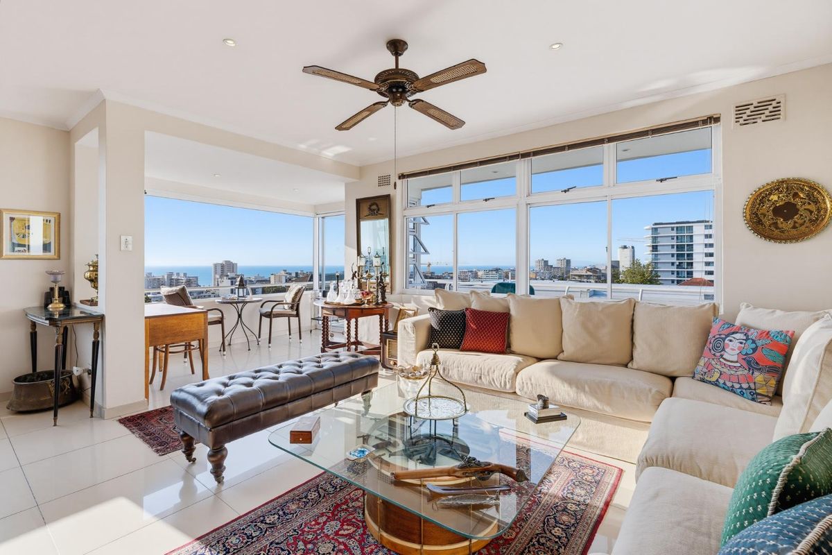 Spacious living room featuring large windows with expansive city and ocean views, tiled flooring, and a ceiling fan.