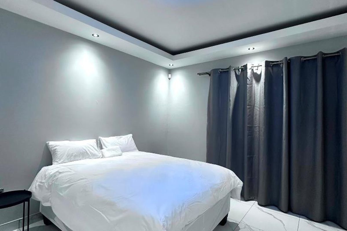 A modern bedroom featuring large-format marble-look floor tiles, recessed ceiling lighting, and a contemporary blue crystal-style flush mount light fixture.