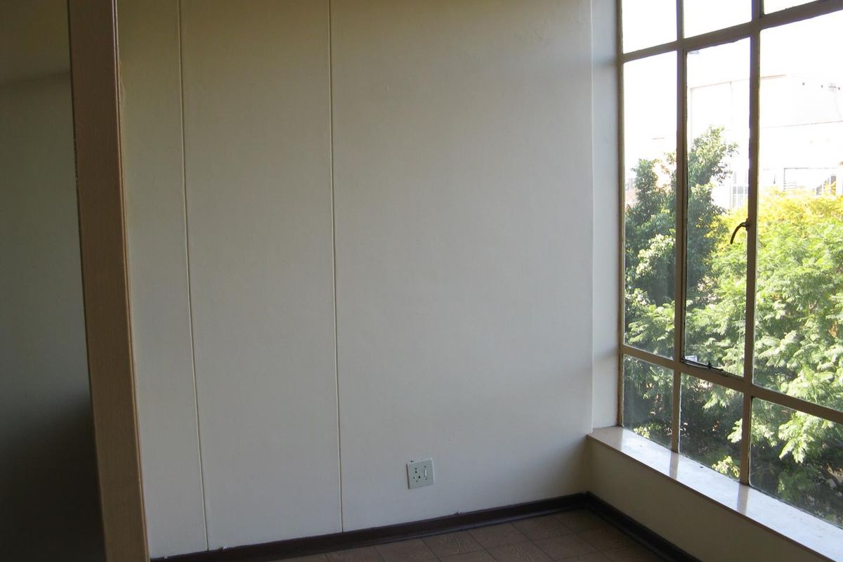 A bright, empty bedroom featuring large metal-framed windows with natural light and tiled flooring.