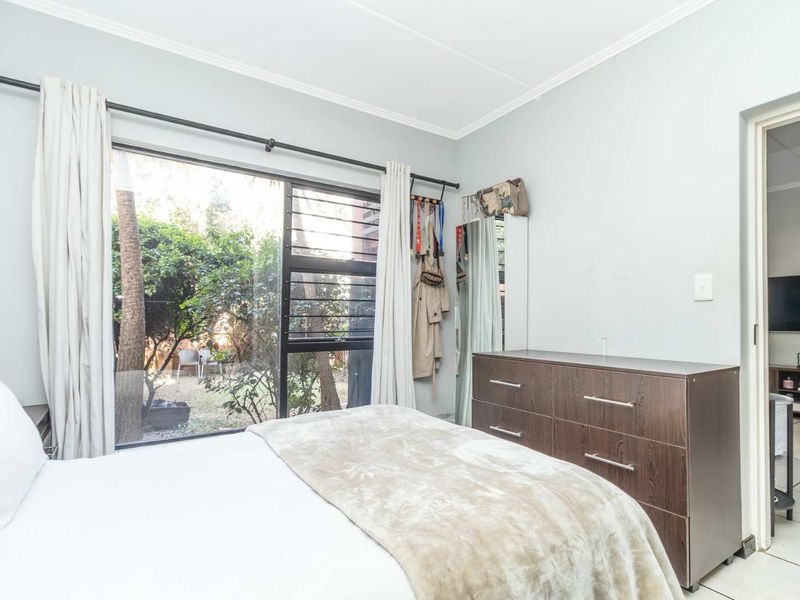 A bedroom featuring large windows with garden views, neutral wall tones, and tiled flooring, offering a bright and functional living space.