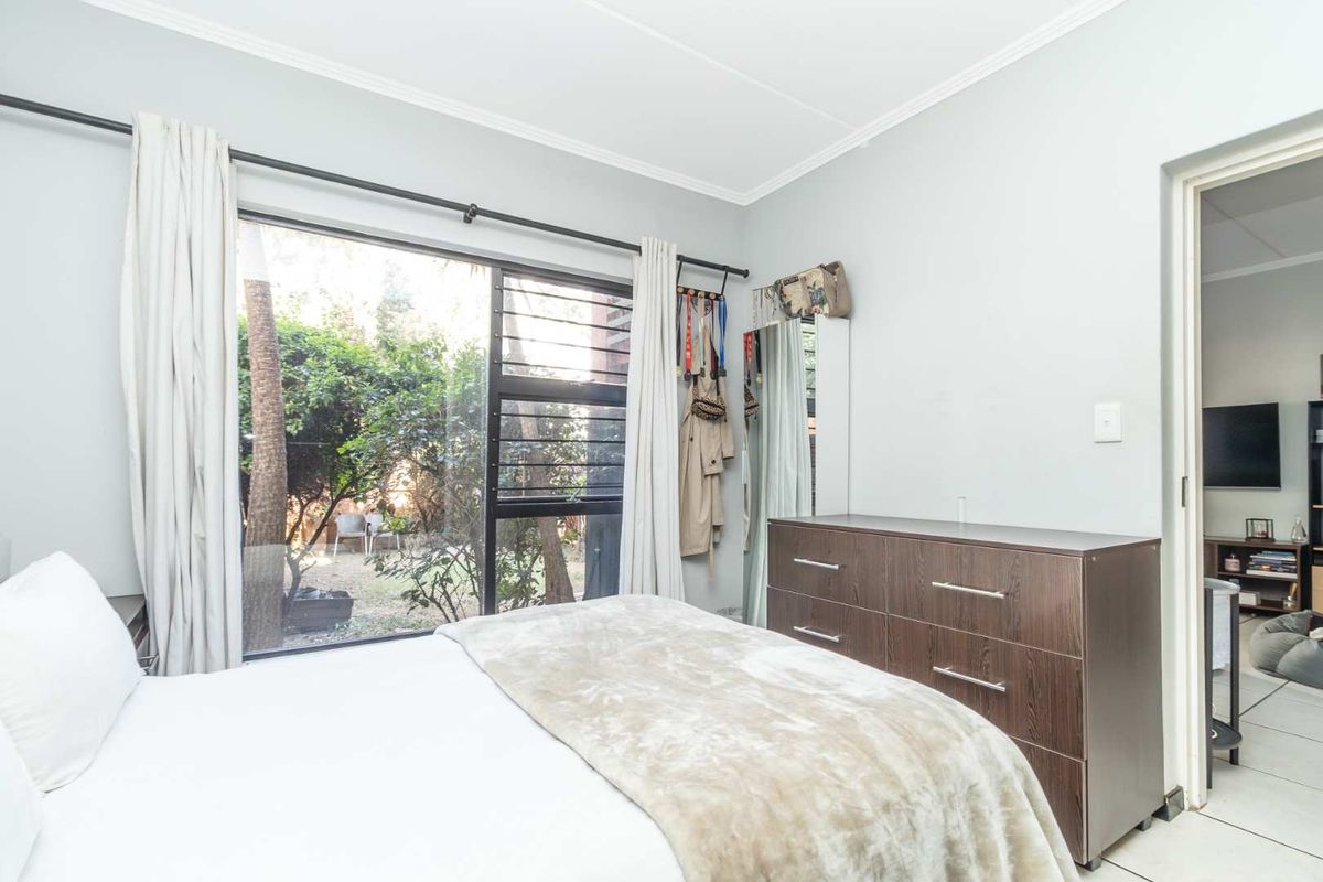 A bedroom featuring large windows with garden views, neutral wall tones, and tiled flooring, offering a bright and functional living space.