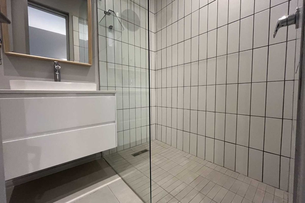 Modern bathroom featuring a walk-in shower with glass partition, white subway wall tiles, and a contemporary wall-mounted vanity unit.