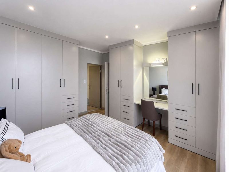 Modern bedroom featuring extensive built-in cabinetry with integrated vanity, recessed lighting, and light-toned laminate flooring.