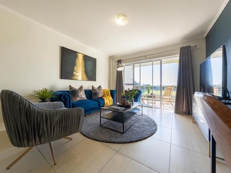 A bright and well-maintained living room featuring large format floor tiles and a sliding glass door providing access to an outdoor balcony area.