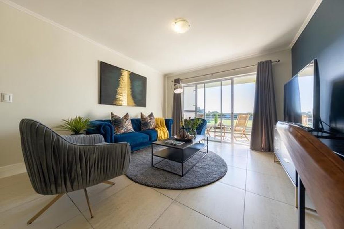 A bright and well-maintained living room featuring large format floor tiles and a sliding glass door providing access to an outdoor balcony area.