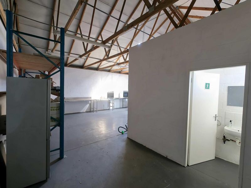 Industrial utility space featuring exposed timber roof trusses, concrete flooring, and a separate partitioned area with a washbasin.