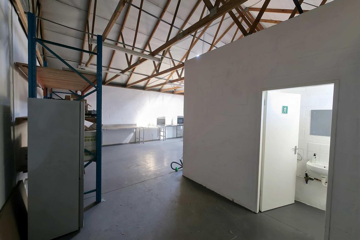 Industrial utility space featuring exposed timber roof trusses, concrete flooring, and a separate partitioned area with a washbasin.