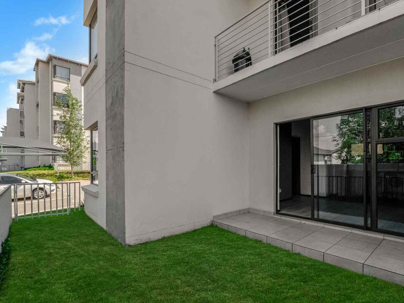A ground floor apartment exterior featuring a private tiled patio, small lawn area, and access to the living space via sliding glass doors.
