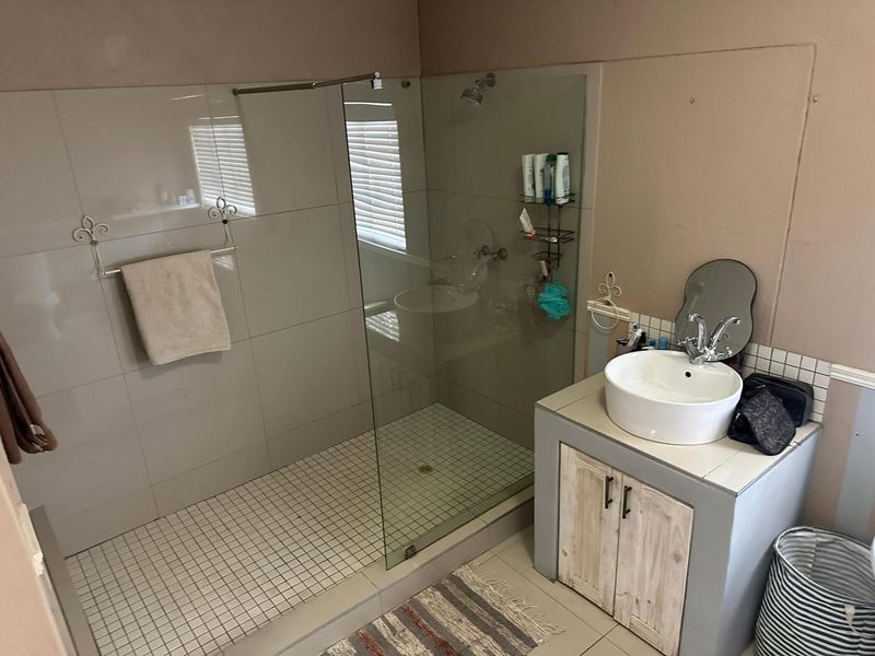 A functional bathroom featuring a walk-in shower with a glass screen, a vessel sink, and a vanity cabinet with tiled finishes.
