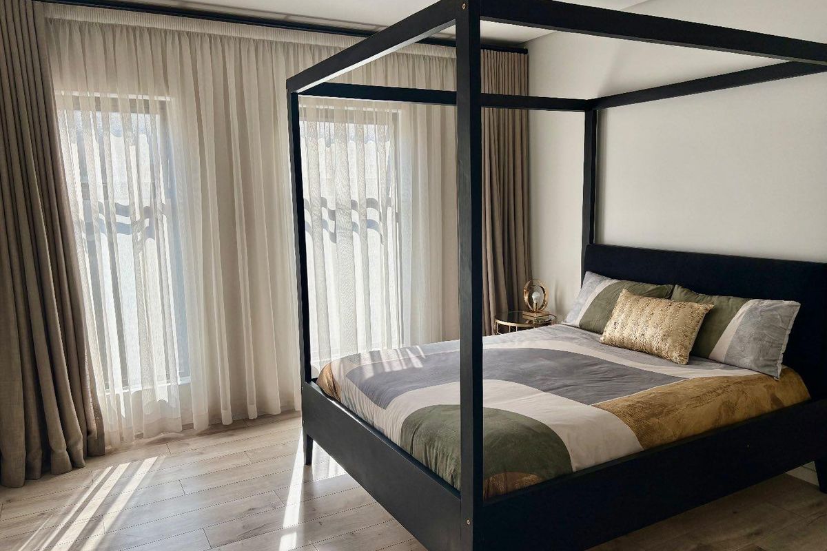 A bright and modern bedroom featuring light wood-look flooring, floor-to-ceiling curtains, and neutral wall finishes.