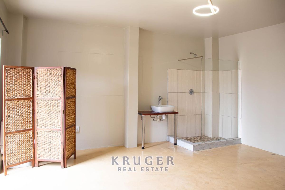A spacious bedroom featuring an open-plan en-suite shower area with a modern vessel sink and glass-enclosed shower stall.