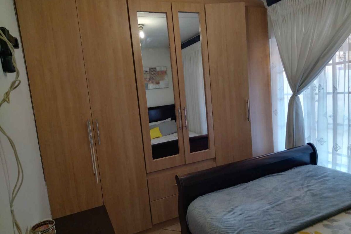A bedroom featuring built-in wooden wardrobes with integrated mirror panels and large windows with curtains.