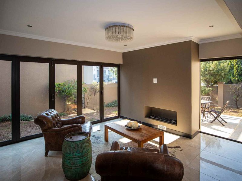 Modern living room featuring large bi-fold doors opening to a patio, a sleek built-in fireplace, polished tile flooring, and an elegant crystal chandelier.