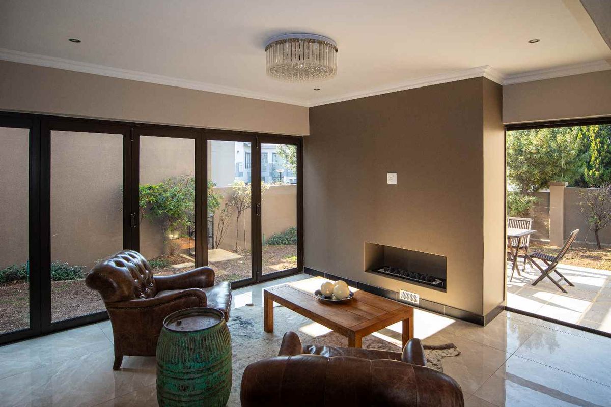 Modern living room featuring large bi-fold doors opening to a patio, a sleek built-in fireplace, polished tile flooring, and an elegant crystal chandelier.