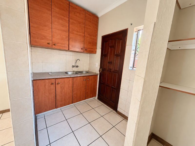 A functional scullery area featuring built-in timber cabinetry, a stainless steel sink, tiled splashbacks, and additional built-in shelving.