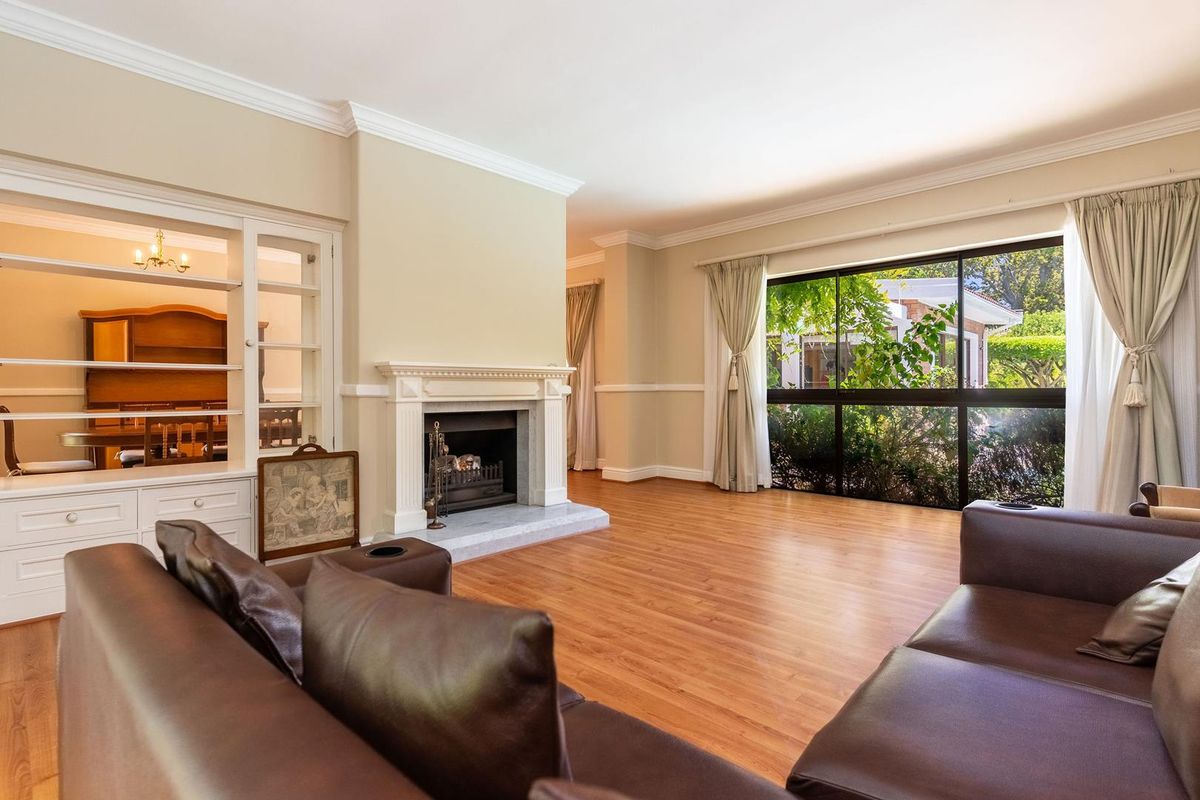 Spacious living room featuring a classic fireplace, built-in display cabinetry, crown molding, and large windows providing natural light and garden views.