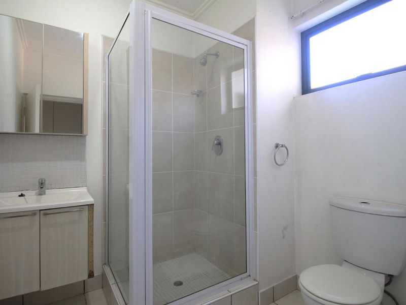 A functional bathroom featuring a glass shower enclosure, vanity cabinet with basin, and a standard toilet, with some visible wear on finishes.