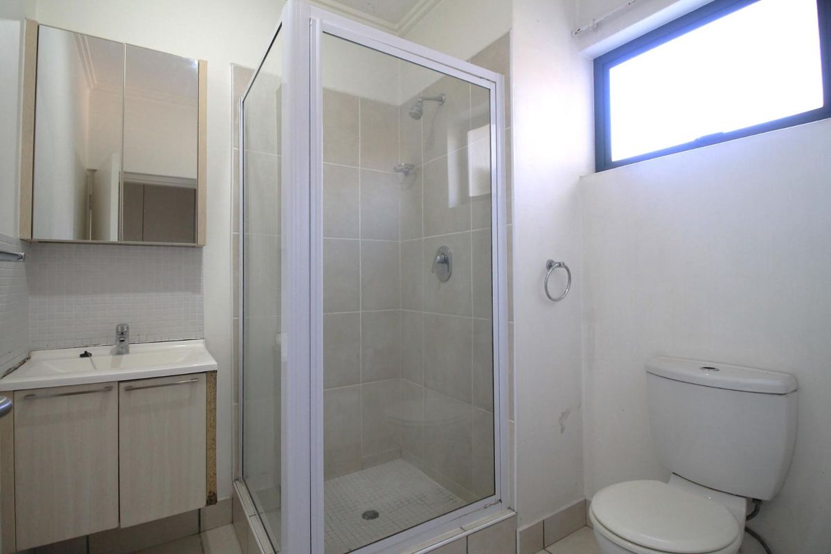 A functional bathroom featuring a glass shower enclosure, vanity cabinet with basin, and a standard toilet, with some visible wear on finishes.