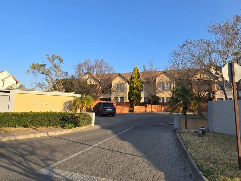 Street view of the apartment complex entrance featuring paved driveway, boundary walls, and established landscaping.