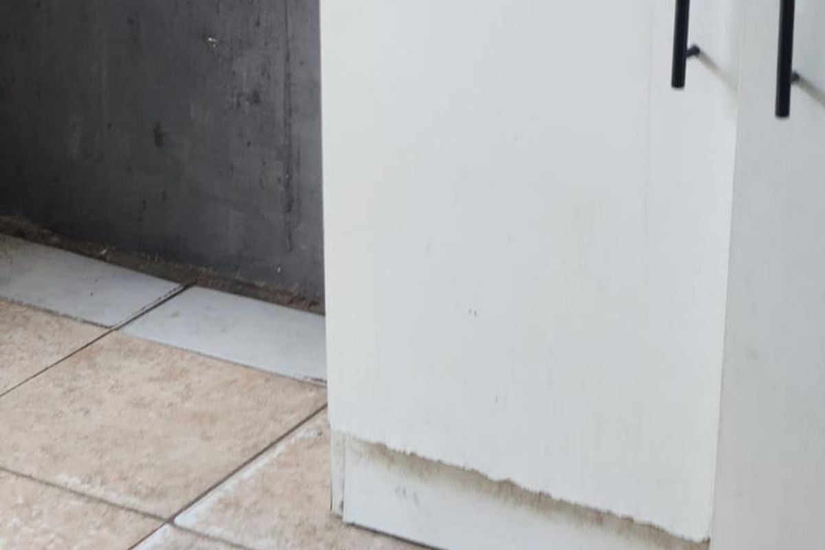Close-up view of kitchen cabinetry showing significant wear and damage to the base finish near the tiled floor.