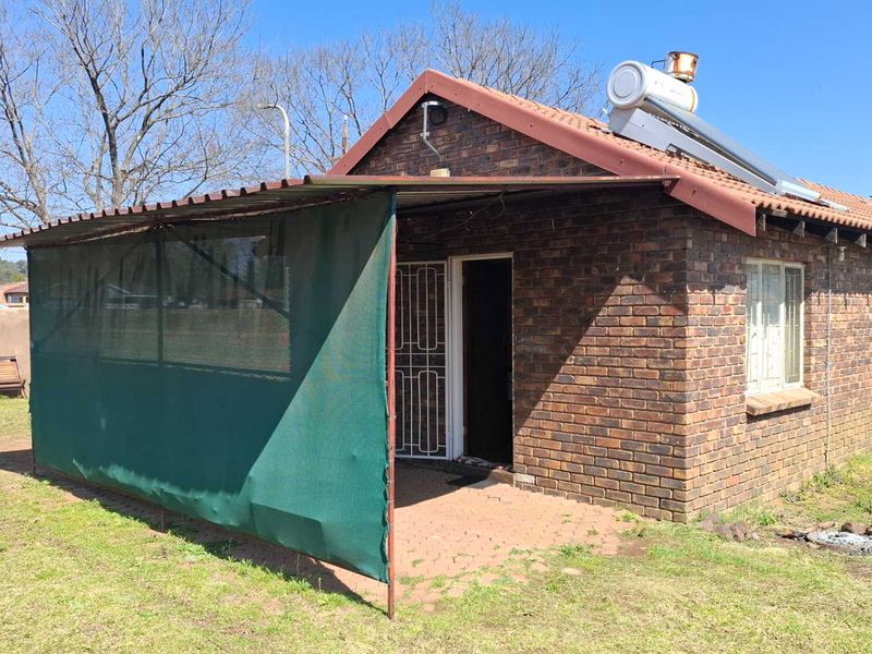 Rear view of a face brick house featuring a covered patio area, solar water heating system, and a surrounding garden space.