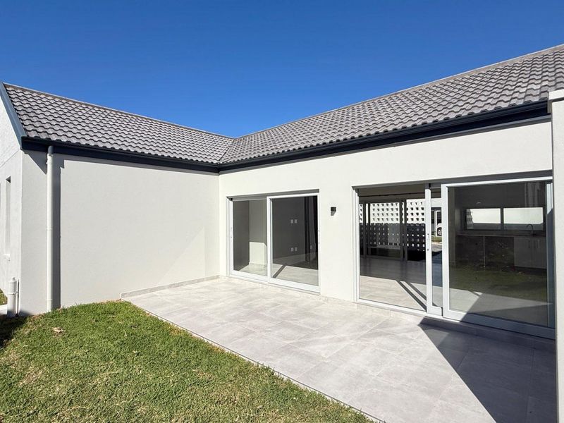 A modern rear exterior view featuring a tiled patio, large sliding glass doors, and a well-maintained lawn under a clear blue sky.
