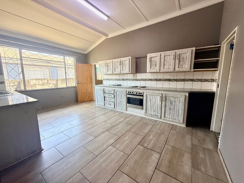 Spacious kitchen featuring built-in cabinetry, integrated oven and hob, tiled backsplash, and large windows with security bars.