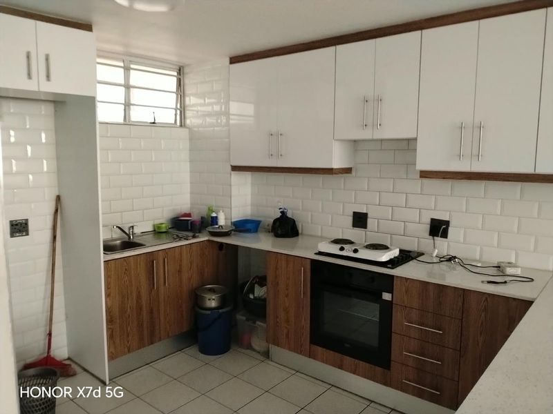 Modern kitchen featuring white subway tile backsplash, wood-finish cabinetry, built-in oven, electric hob, and tiled flooring.
