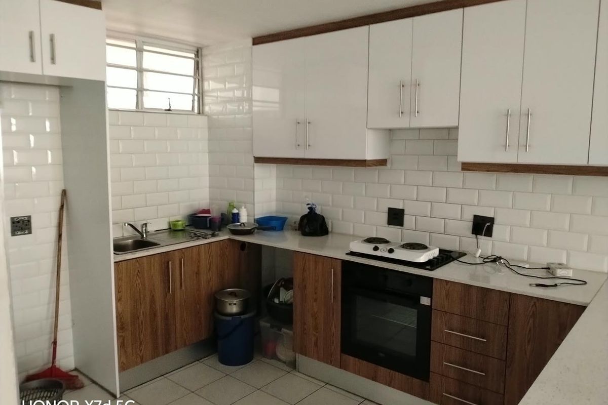 Modern kitchen featuring white subway tile backsplash, wood-finish cabinetry, built-in oven, electric hob, and tiled flooring.