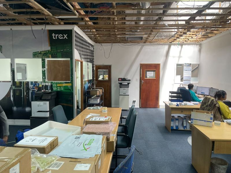 An industrial office space featuring exposed ceiling joists, carpeted flooring, and partitioned work areas, currently requiring ceiling completion and general refurbishment.