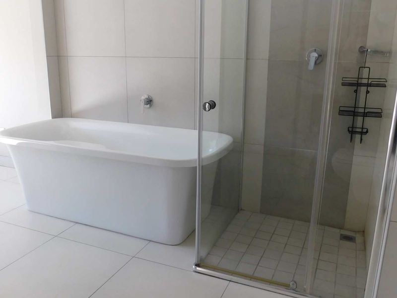 Modern bathroom featuring a sleek freestanding bathtub and a separate glass-enclosed shower with neutral floor-to-ceiling tiling.