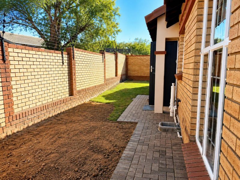 Rear exterior view featuring a face brick boundary wall with electric fencing, a paved walkway, and an unlandscaped garden area.
