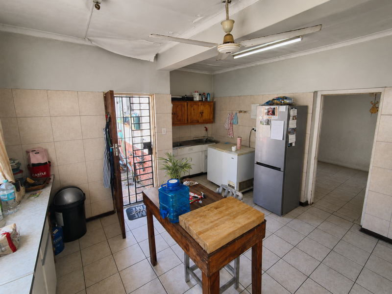 A functional kitchen space featuring tiled walls and flooring, built-in cabinetry, and a ceiling fan, requiring cosmetic updates to the ceiling and finishes.