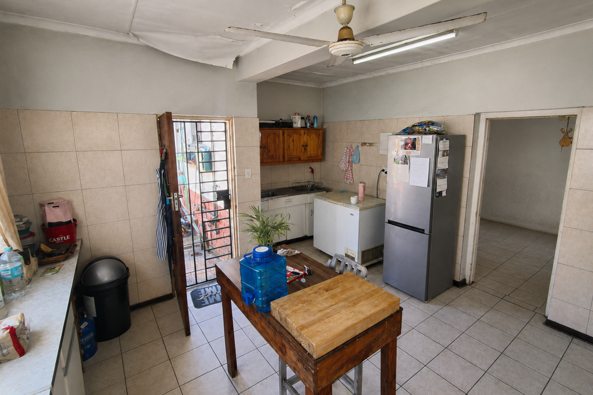 A functional kitchen space featuring tiled walls and flooring, built-in cabinetry, and a ceiling fan, requiring cosmetic updates to the ceiling and finishes.