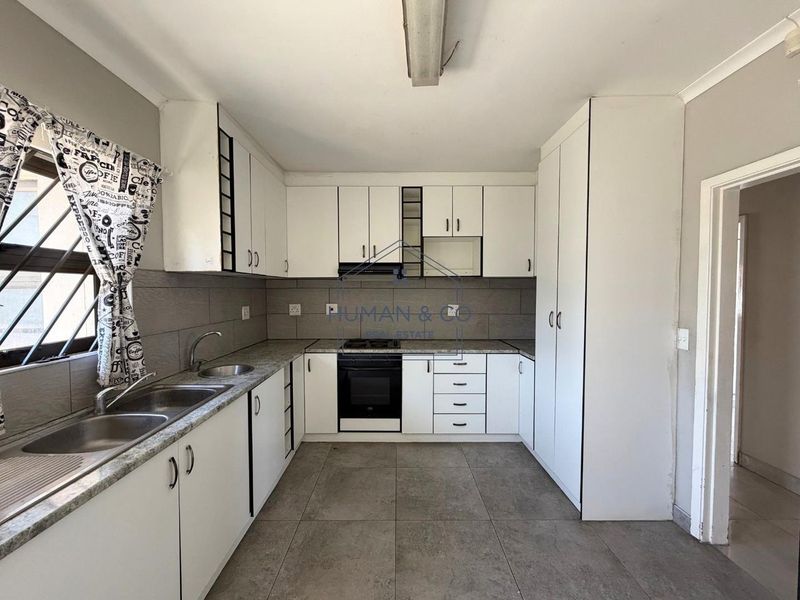 A functional kitchen featuring white built-in cabinetry, granite countertops, a double sink, and integrated oven with hob, finished with neutral floor tiles.