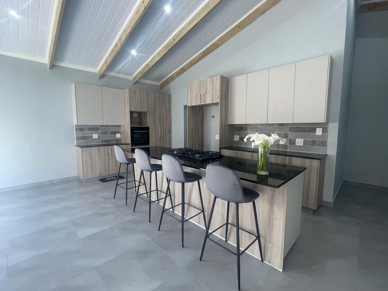 Modern kitchen featuring sleek cabinetry, stone countertops, a central island with a gas hob, and striking exposed timber ceiling beams.