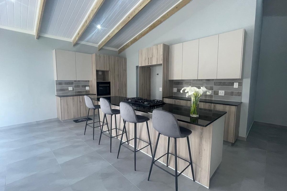 Modern kitchen featuring sleek cabinetry, stone countertops, a central island with a gas hob, and striking exposed timber ceiling beams.