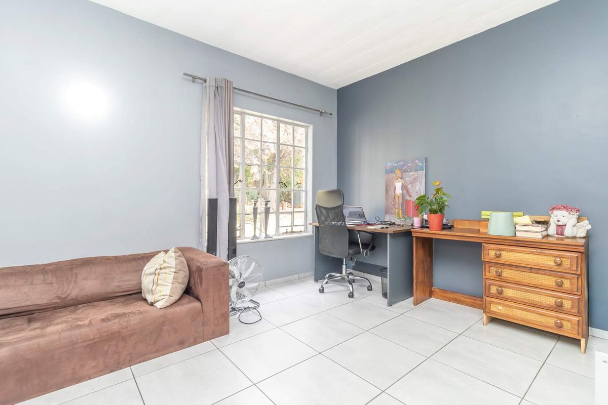 A functional bedroom or home office space featuring tiled flooring, large windows, and neutral wall finishes.