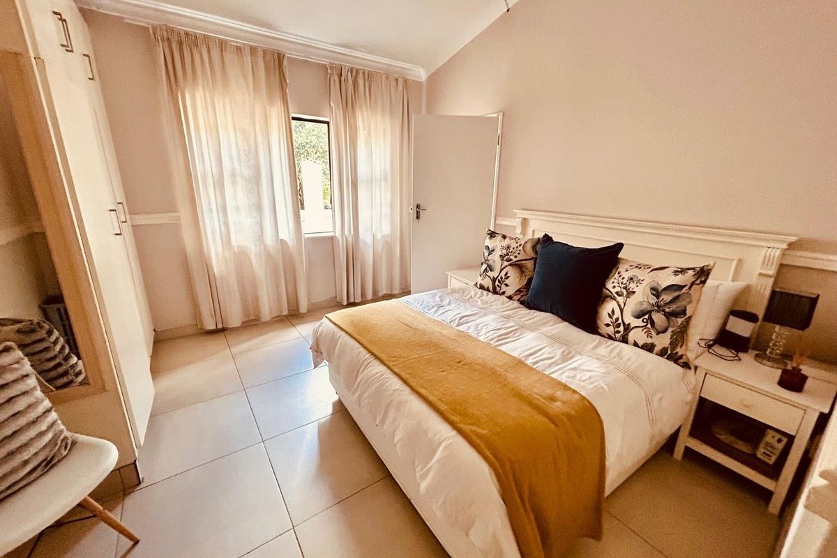 A well-lit bedroom featuring built-in cupboards, tiled flooring, and large windows allowing for natural light.