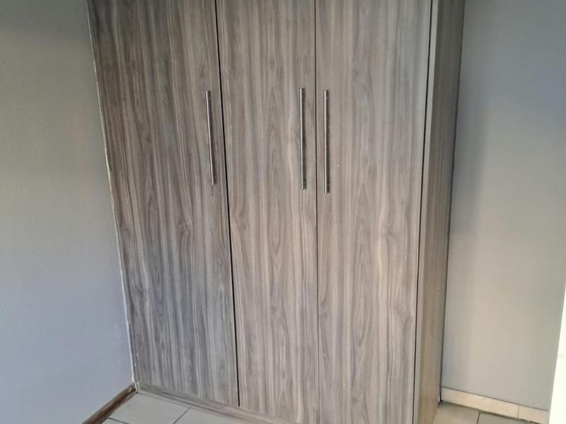 A clean bedroom space featuring neutral tiled flooring and a modern wood-grain finish built-in wardrobe.
