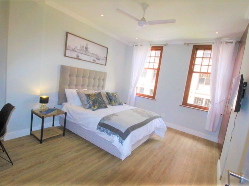 A well-lit bedroom featuring laminate flooring, a ceiling fan, and built-in cupboards, offering a comfortable and functional living space.