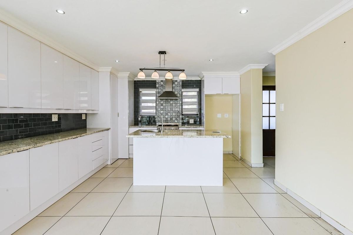 Modern kitchen featuring white cabinetry, granite countertops, a central island, and a decorative tiled backsplash with a built-in extractor fan.