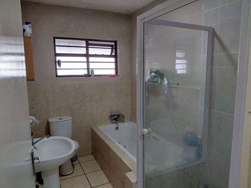 A functional bathroom featuring a pedestal basin, toilet, built-in bathtub, and a separate shower enclosure with tiled finishes.