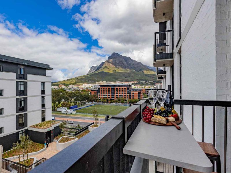 A modern apartment balcony featuring a built-in stone bar counter and metal railing, offering scenic mountain and urban views.