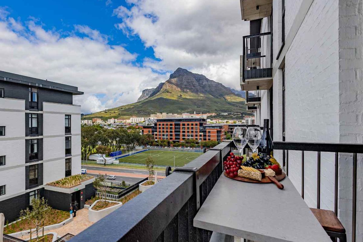 A modern apartment balcony featuring a built-in stone bar counter and metal railing, offering scenic mountain and urban views.