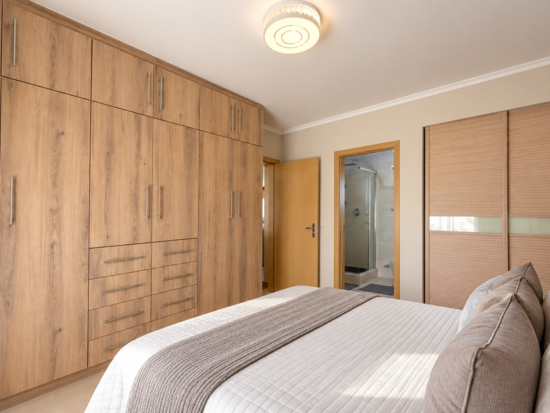 A well-maintained bedroom featuring extensive floor-to-ceiling wood-finish built-in cabinetry, a modern ceiling light, and direct access to an en-suite bathroom.