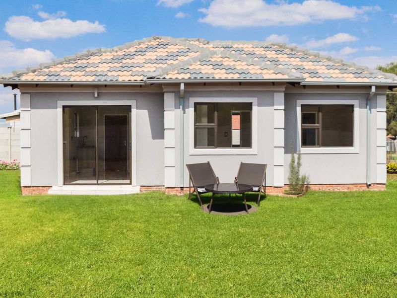 Rear view of a single-story house featuring a tiled roof, plastered exterior walls, and sliding glass doors leading to a well-maintained lawn.
