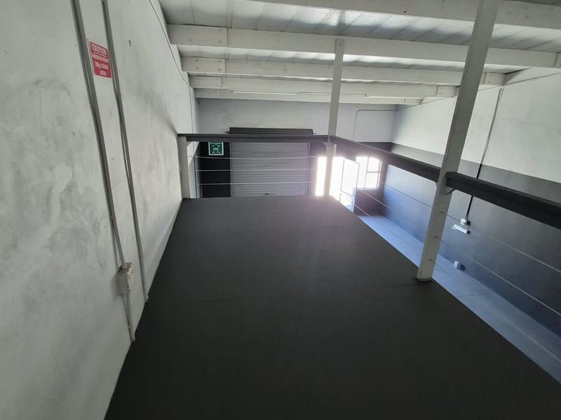 Industrial mezzanine level featuring exposed steel beams, high ceilings, and a roller shutter door, suitable for storage or additional workspace.