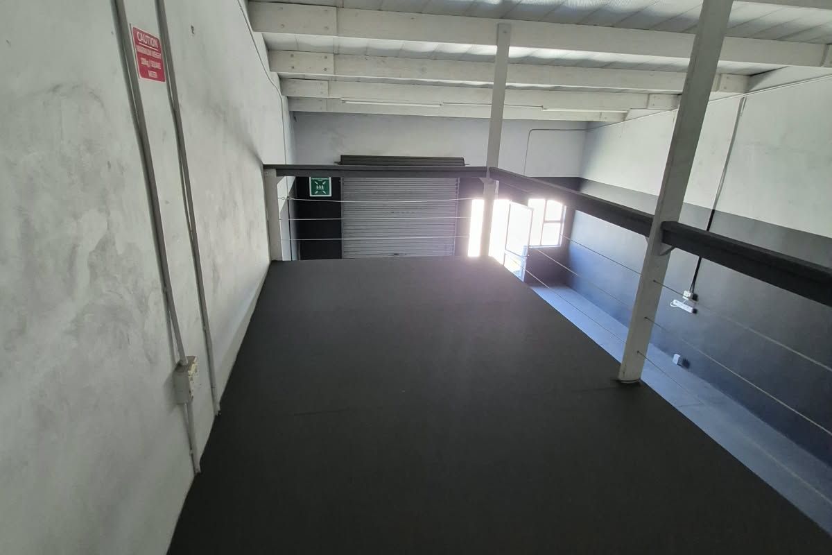 Industrial mezzanine level featuring exposed steel beams, high ceilings, and a roller shutter door, suitable for storage or additional workspace.